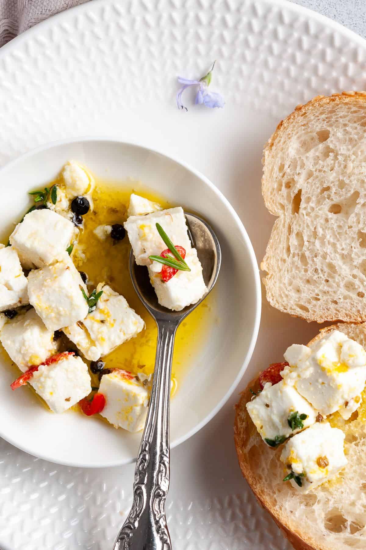 Up close shot of dish of feta, with spoon in it, and some slices of bread around the edge.