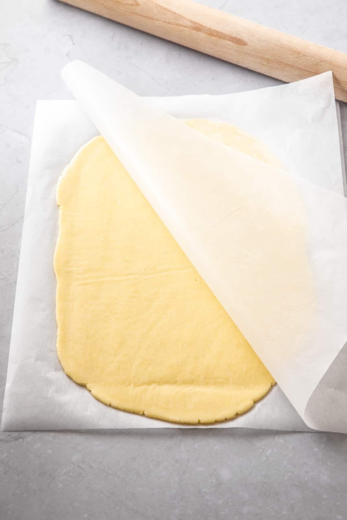 Rolled pastry, between two sheets of baking paper, with a rolling pin alongside.