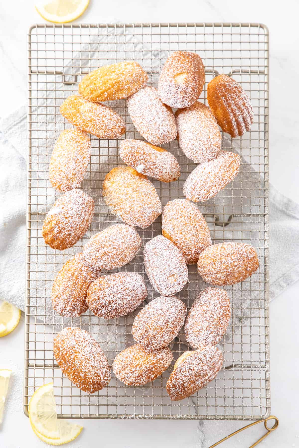 Overhead shot of Madeleines dusted with icing sugar sitting on a cooling rack.