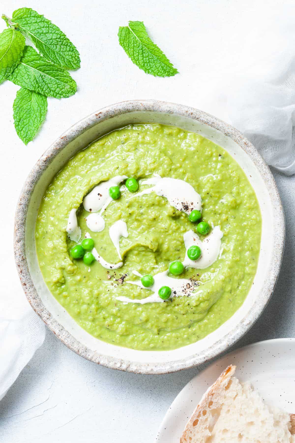 Bowl of soup, garnished with some cream and peas, with a spoon sitting in bowl.