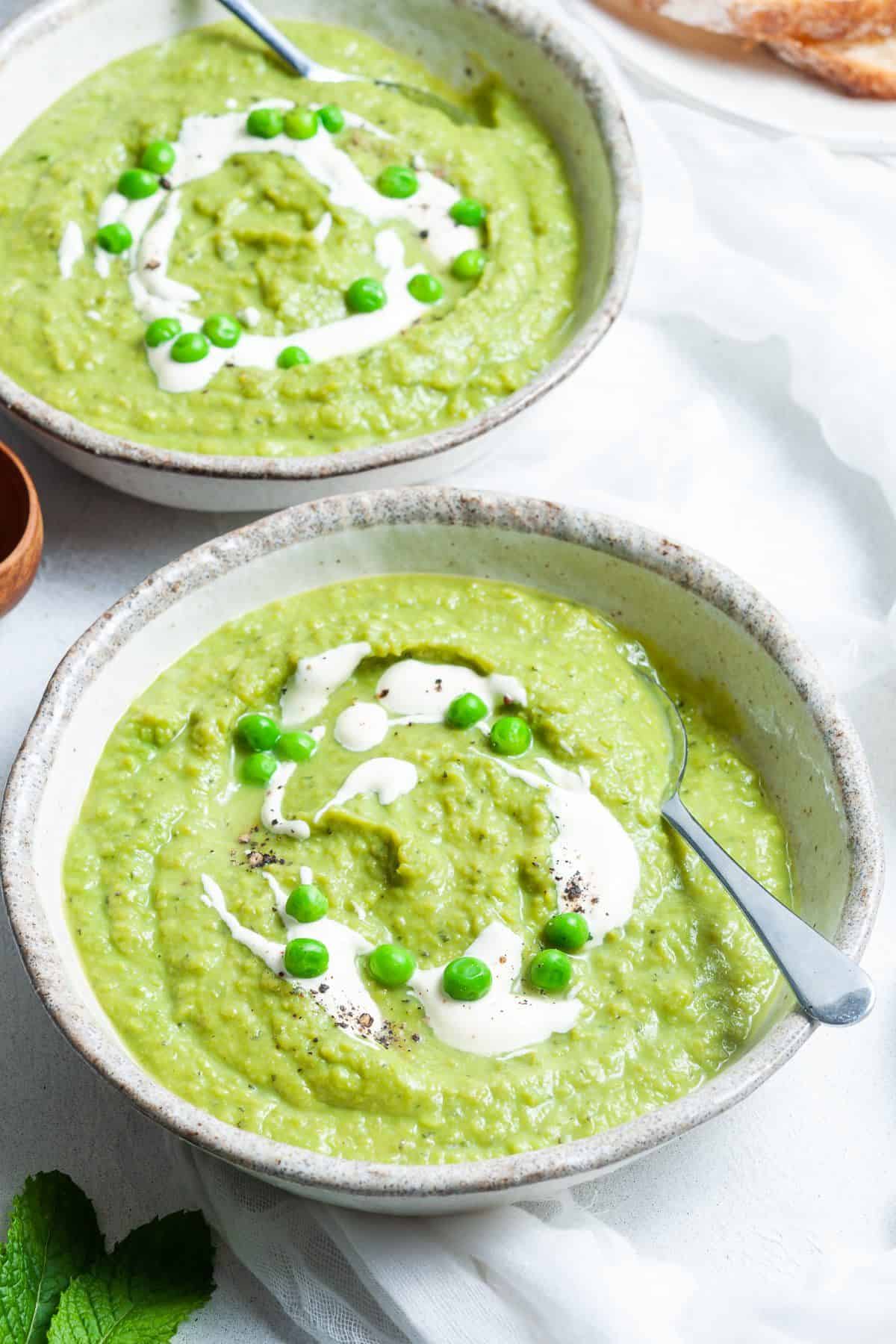 Two bowls of soup, garnished with some cream and peas, with a spoon sitting in each bowl.