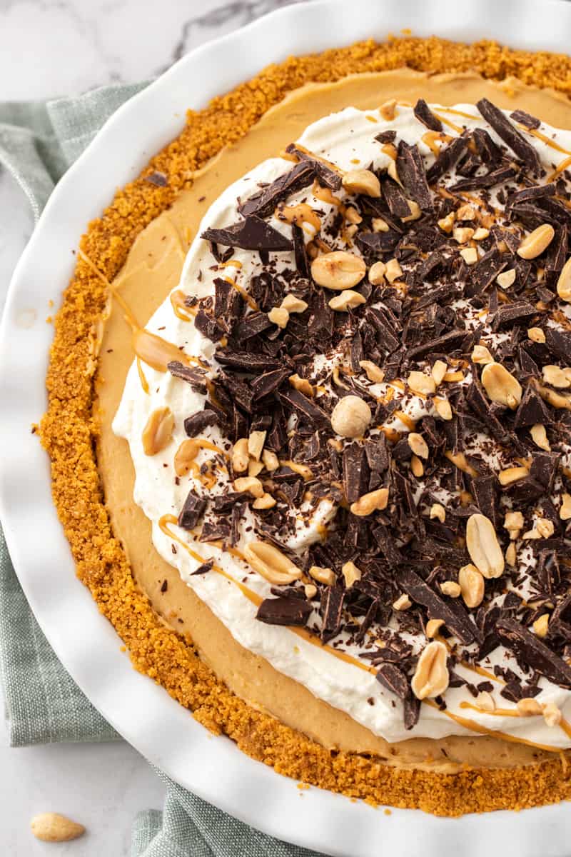 Overhead shot of pie in dish, decorated with cream, chocolate and peanuts.