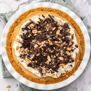 Overhead shot of pie in dish, decorated with cream, chocolate and peanuts.