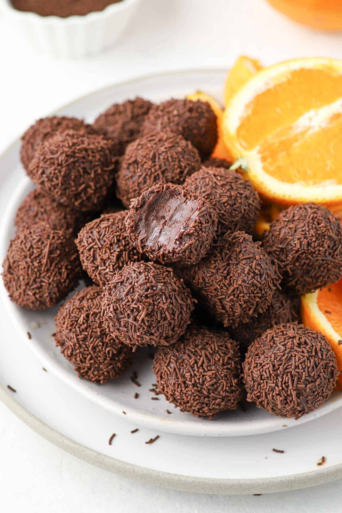 Plate of truffles, garnished with some orange slices, and one truffle missing a bite.