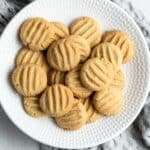 Round white plate of cookies, sitting on a grey tea towel.