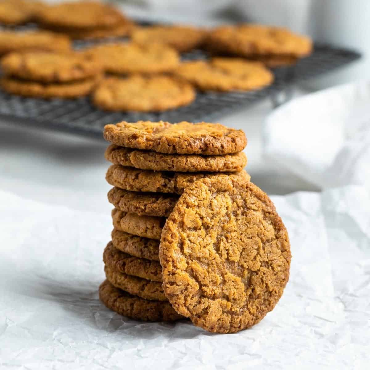 Stack of cookies sitting on some baking paper, with tray of cookies in background.