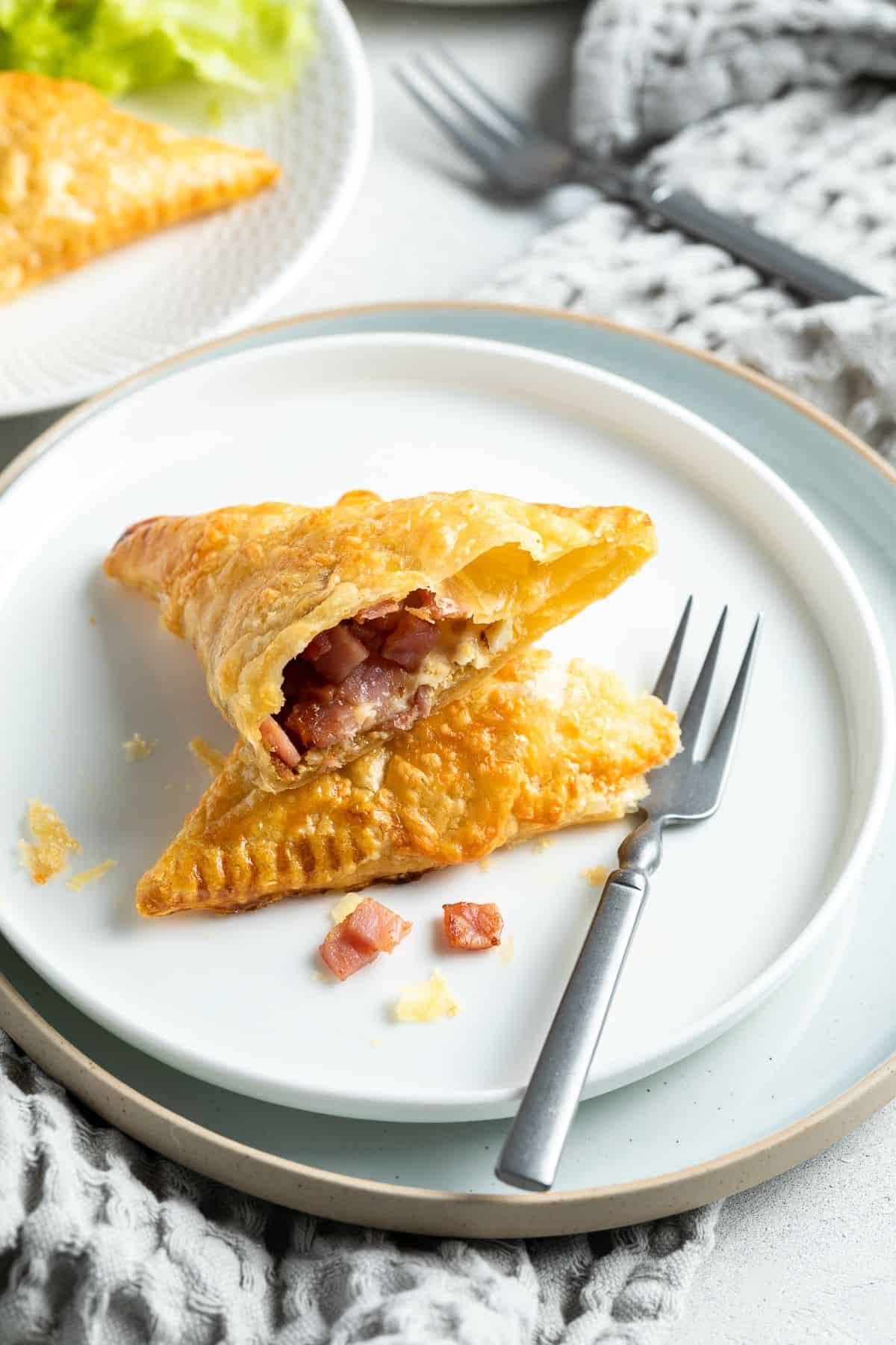 A bacon turnover cut in half, sitting on a white plate with a fork on the side.