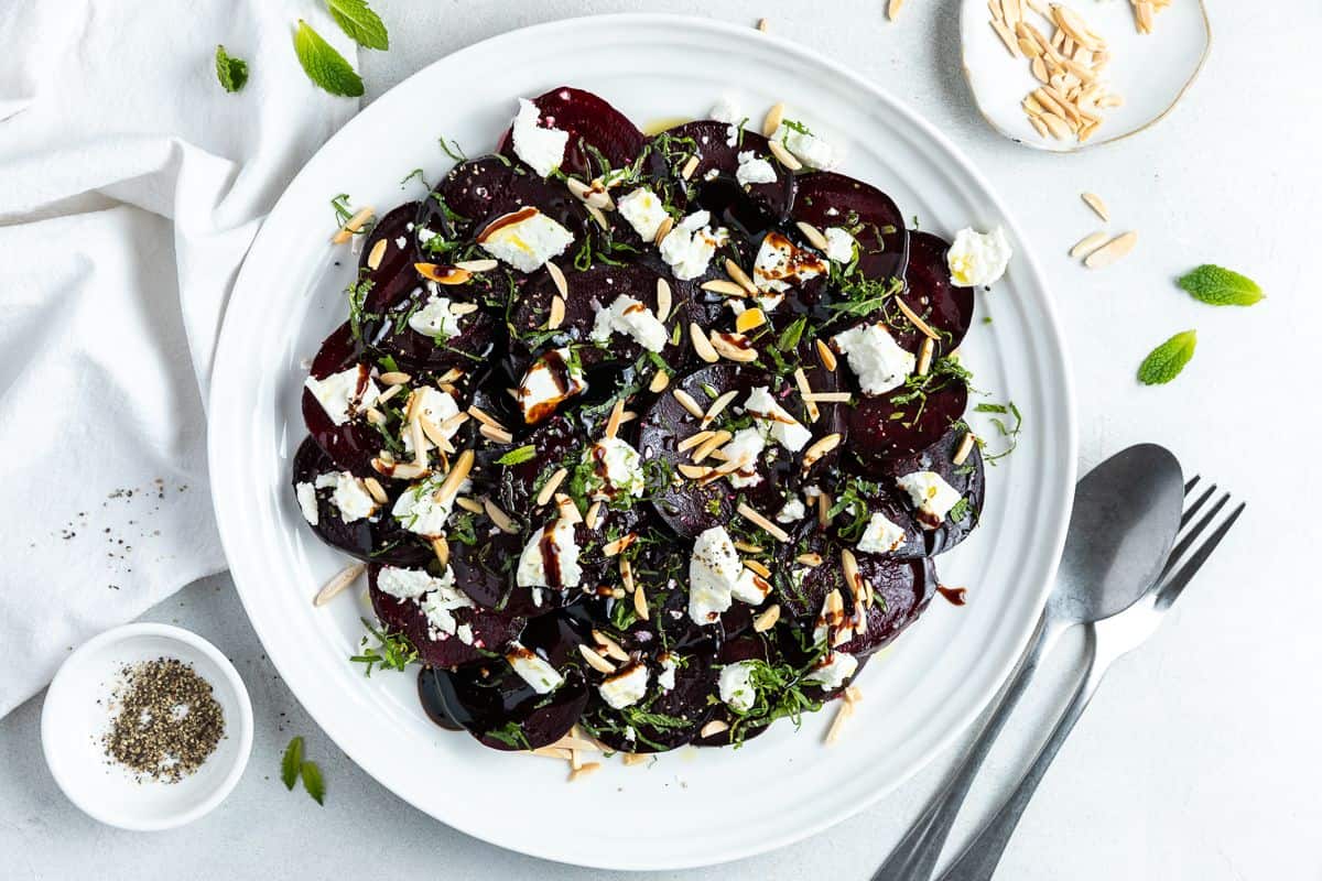 Round white plate with beetroot salad, with some cutlery on the edge.