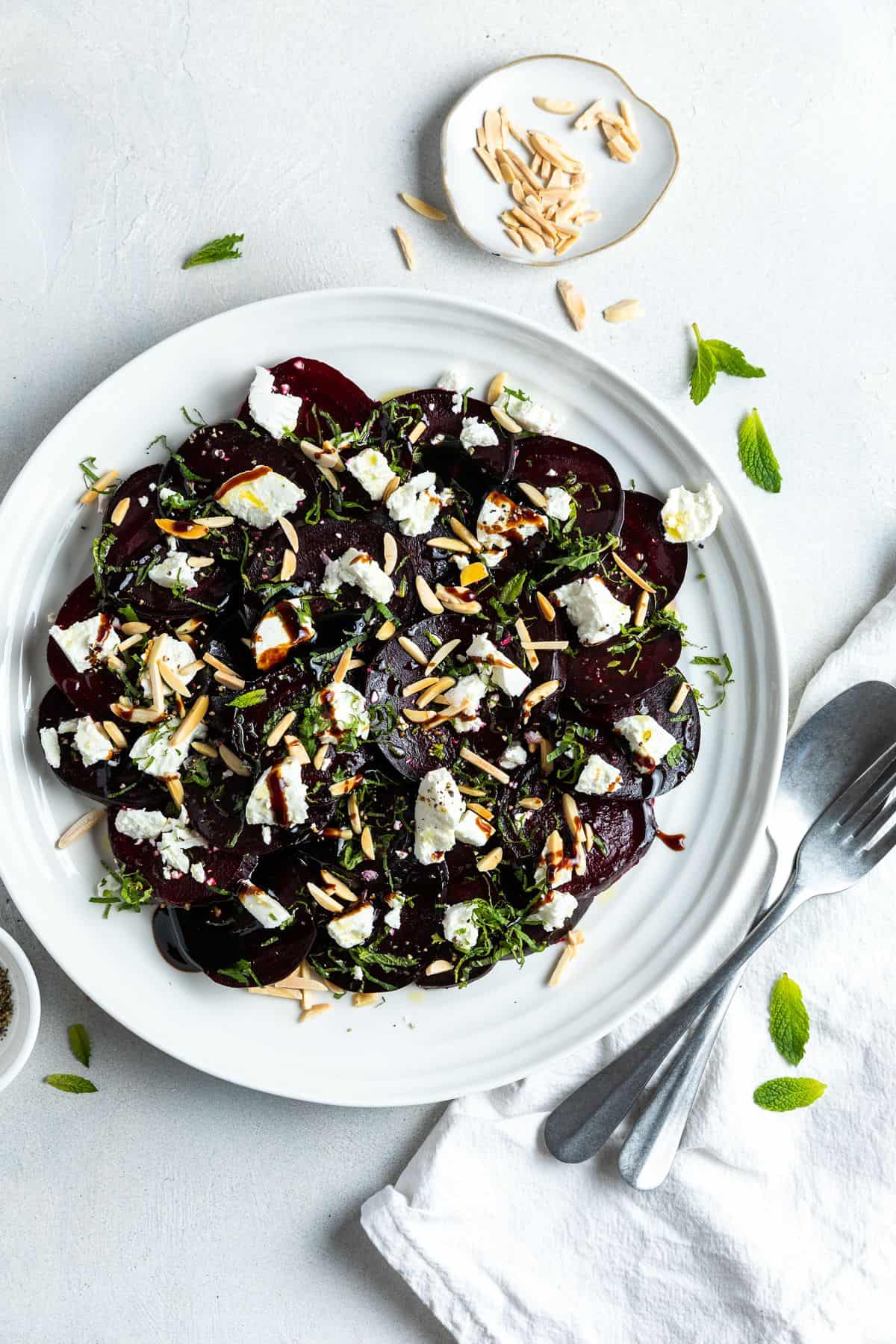 Overhead shot of round white plate with beetroot salad, with some cutlery on the edge.