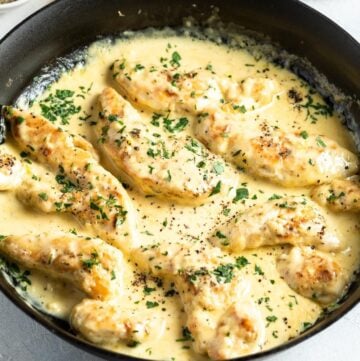Up close shot of dish of chicken in cream sauce sprinkled with parsley.