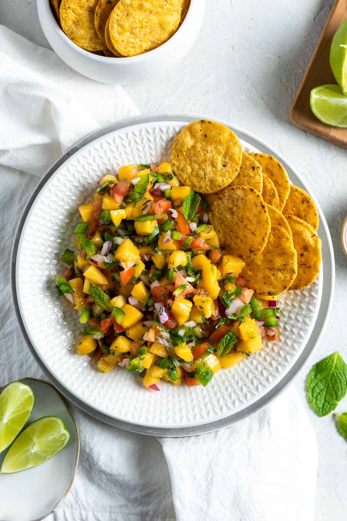 Round white dish of mango salsa with some corn chips on the edge.