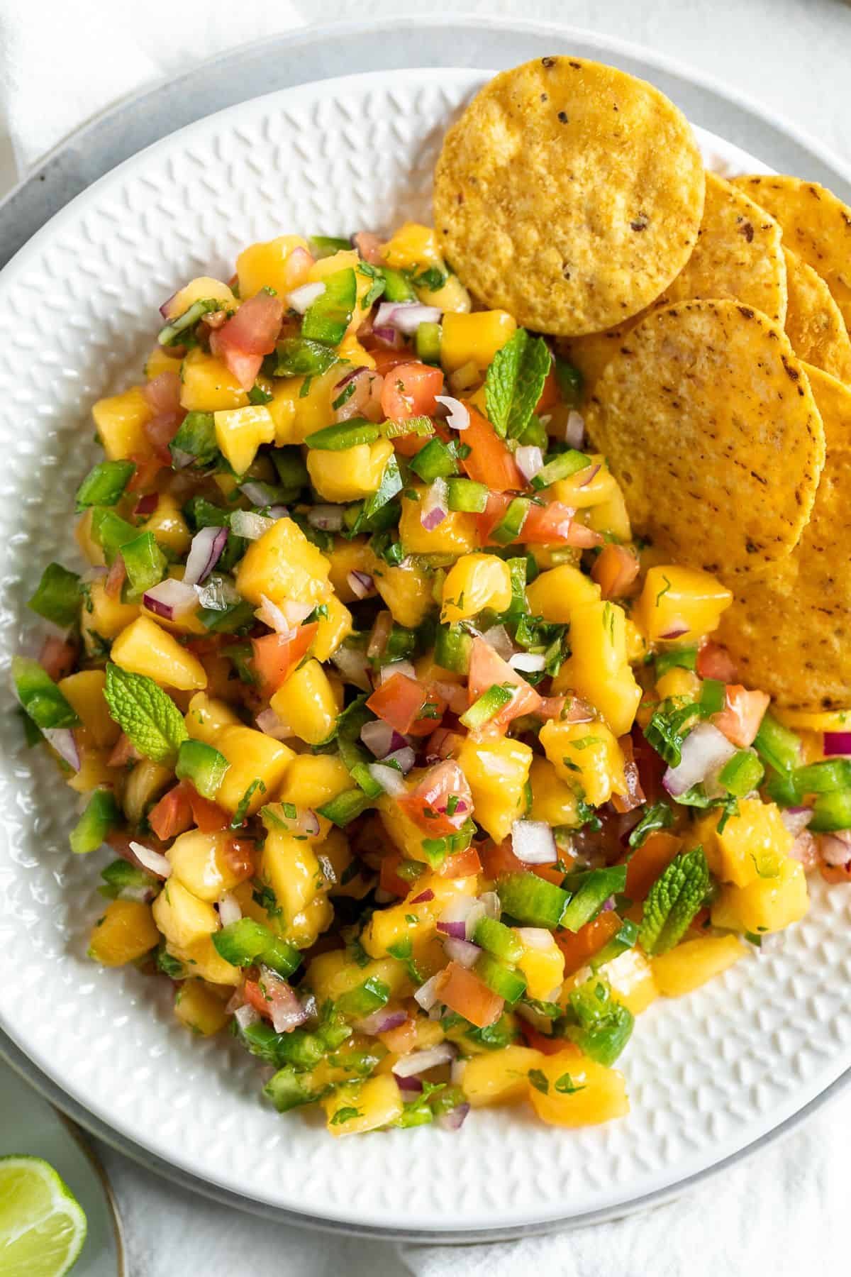 Round white dish of mango salsa with some corn chips on the edge.