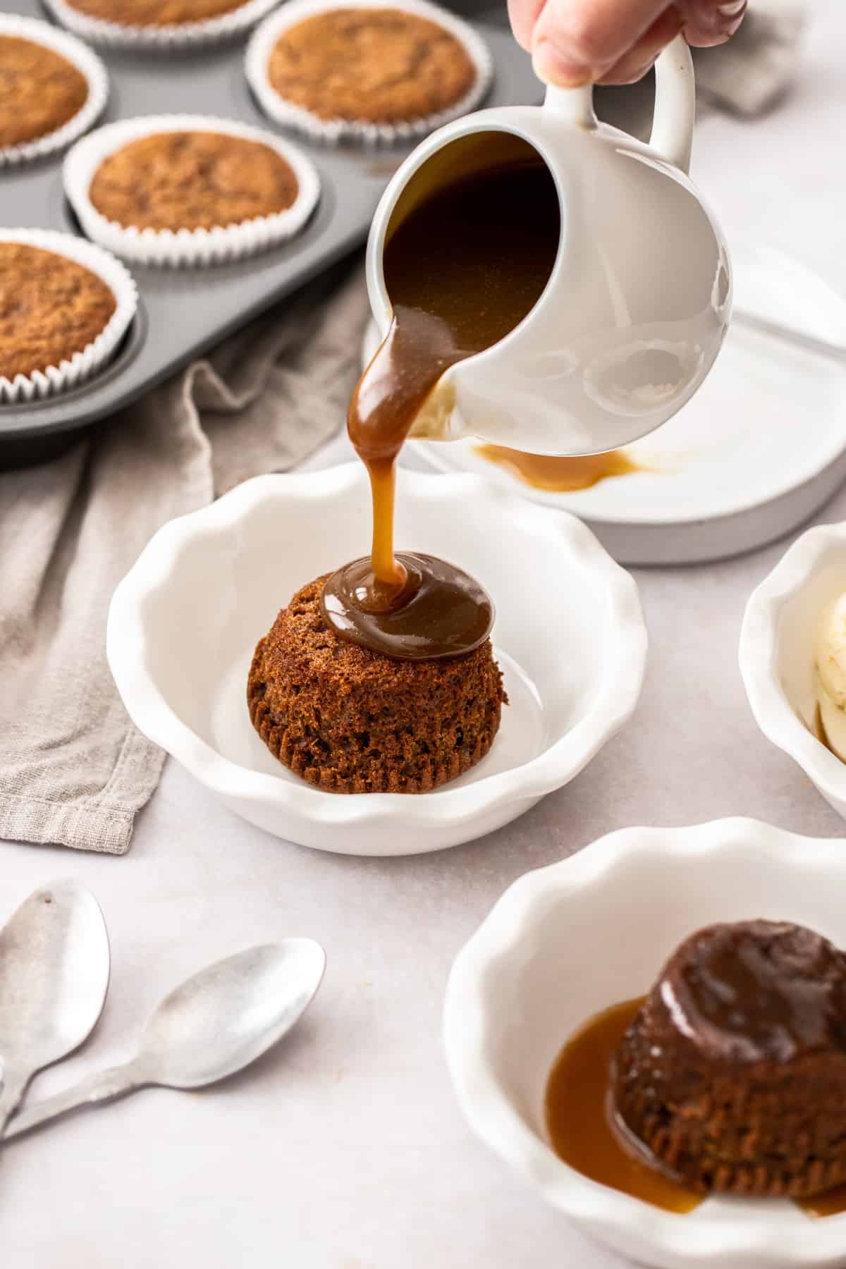 A pudding in a small dish, with some toffee sauce being poured over it.