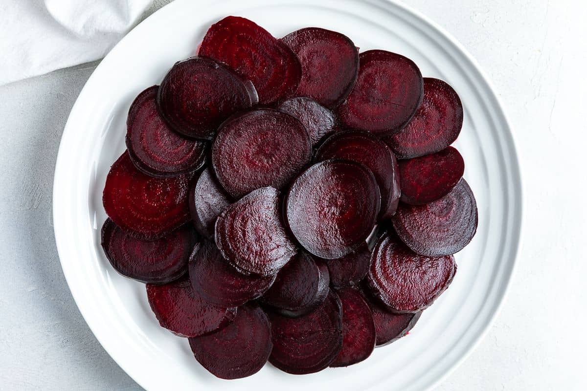 Sliced roasted beetroot on a round white plate.