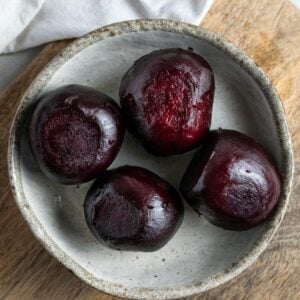 Four cooked beetroot in a dish sitting on a wooden board