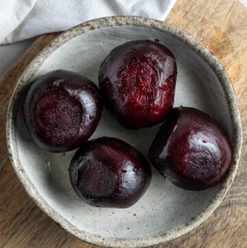 Four cooked beetroot in a dish sitting on a wooden board