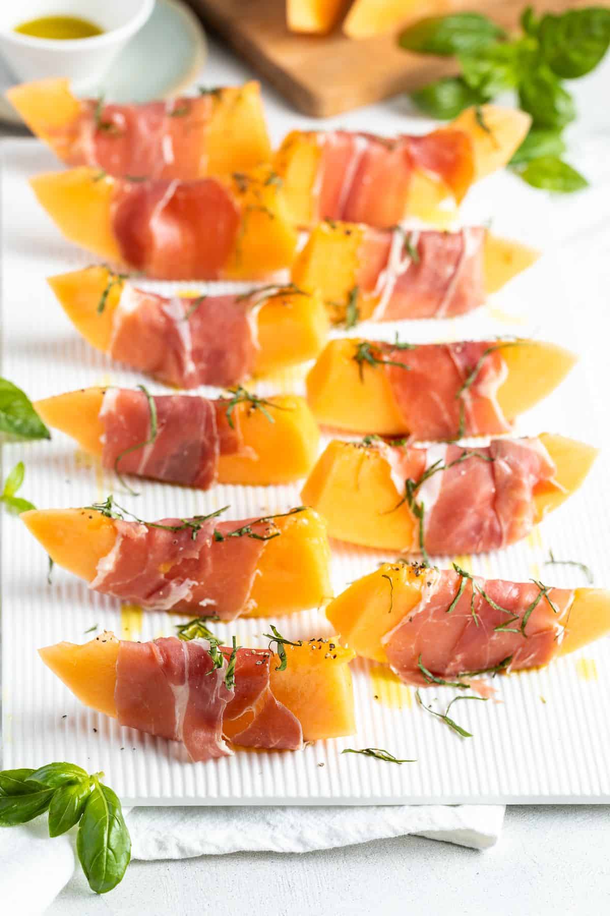 Slices of prosciutto wrapped melon sitting on a white serving platter.