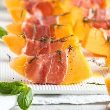 Slices of prosciutto wrapped melon sitting on a white serving platter.
