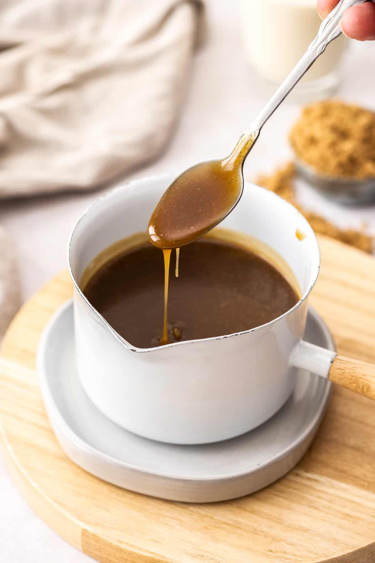 Small white pot of toffee sauce, with a spoon dipping into it.