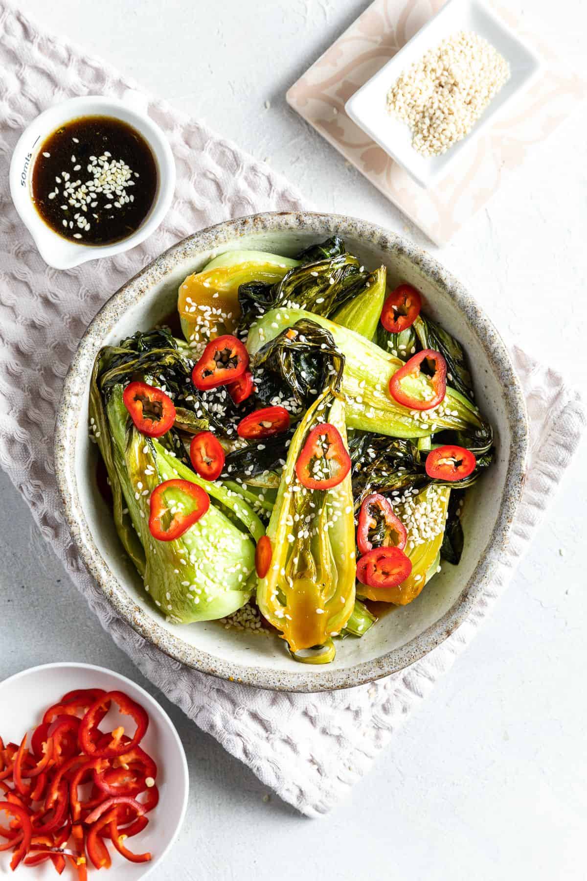 Round serving dish of bok choy, garnished with sesame seeds and fresh chilli.