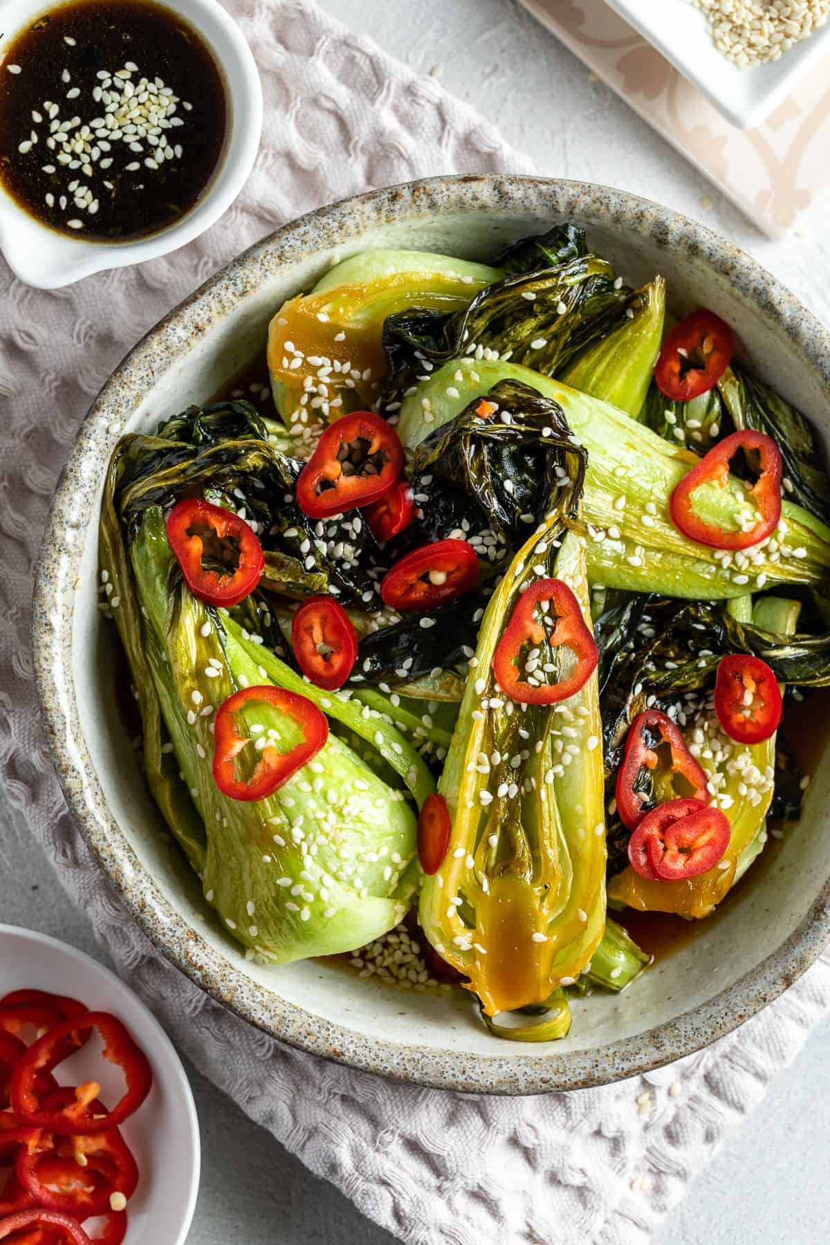 Round serving dish of bok choy, garnished with sesame seeds and fresh chilli.