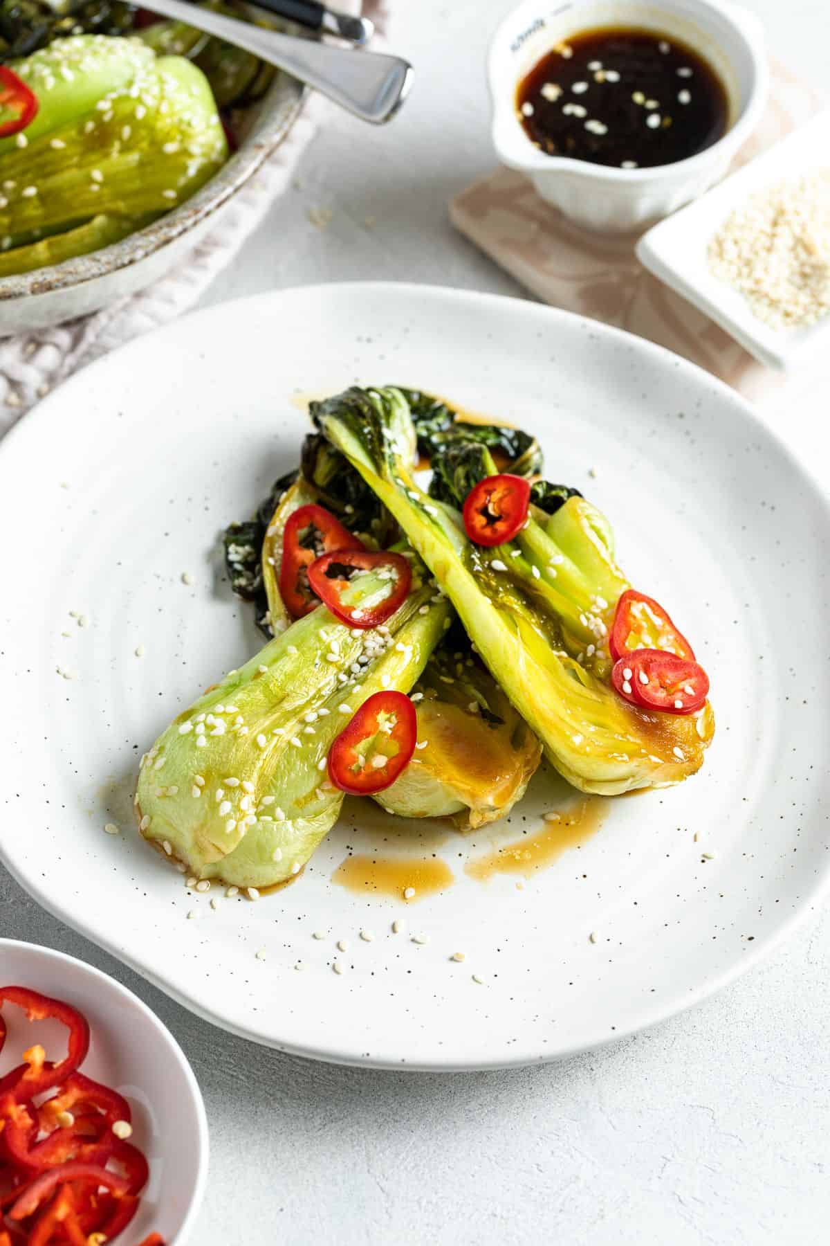 A serve of roasted bok choy on a round white plate, garnished with sesame seeds and chilli.