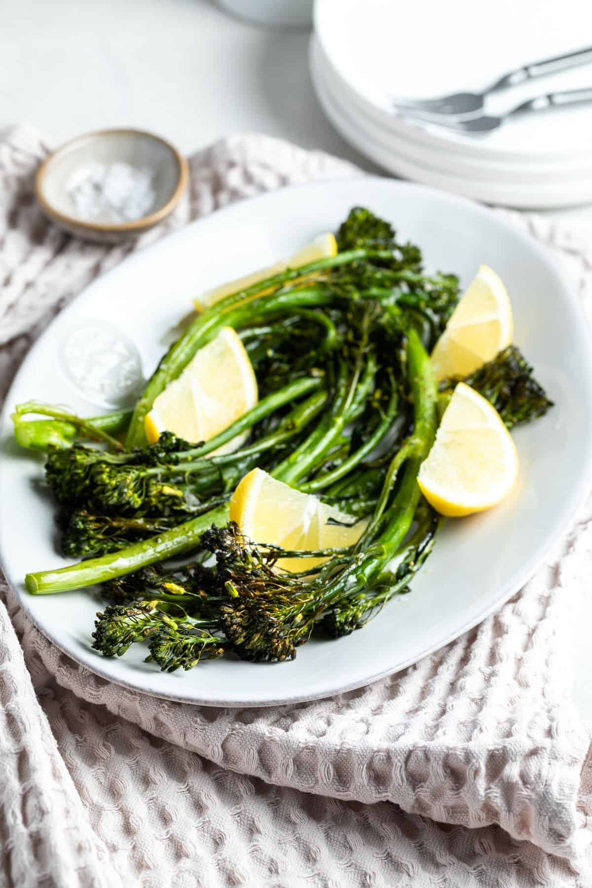 White dish with cooked broccolini garnished with lemon wedges.