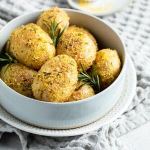 Round dish of roasted potatoes garnished with some rosemary leaves.