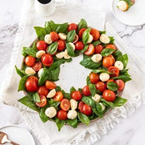 Caprese salad in a wreath circle, on a white plate, sitting on a white cloth, with a jug of balsamic glaze in the background.