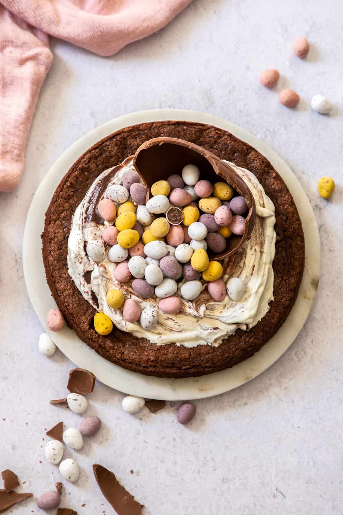 Whole cake sitting on a plate, decorated with cream and Easter chocolates.
