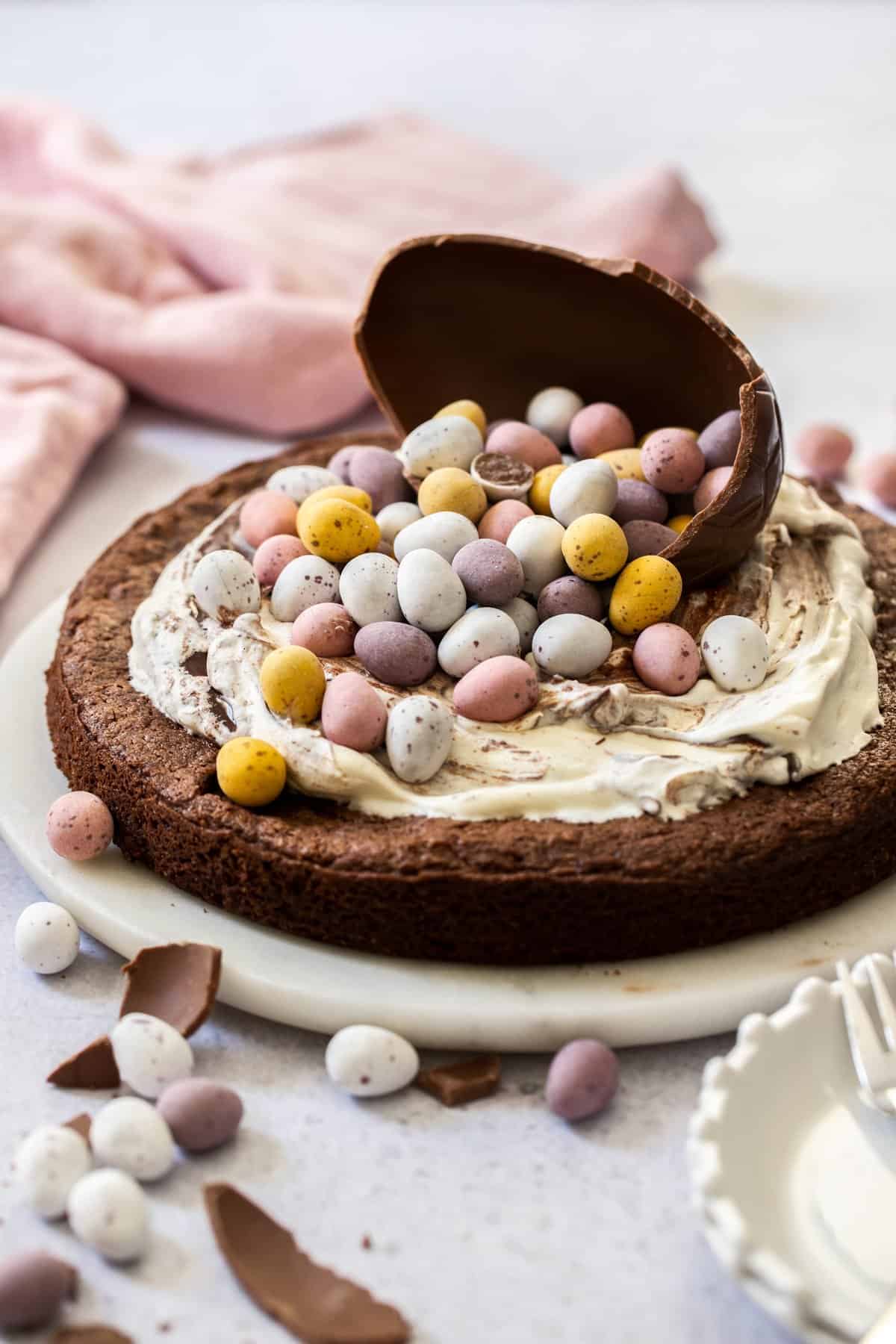Whole cake sitting on a plate, decorated with cream and Easter chocolates.