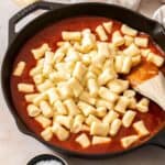 Skillet with a tomato sauce and the ricotta gnocchi sitting on top, with a wooden spoon about to combine them.