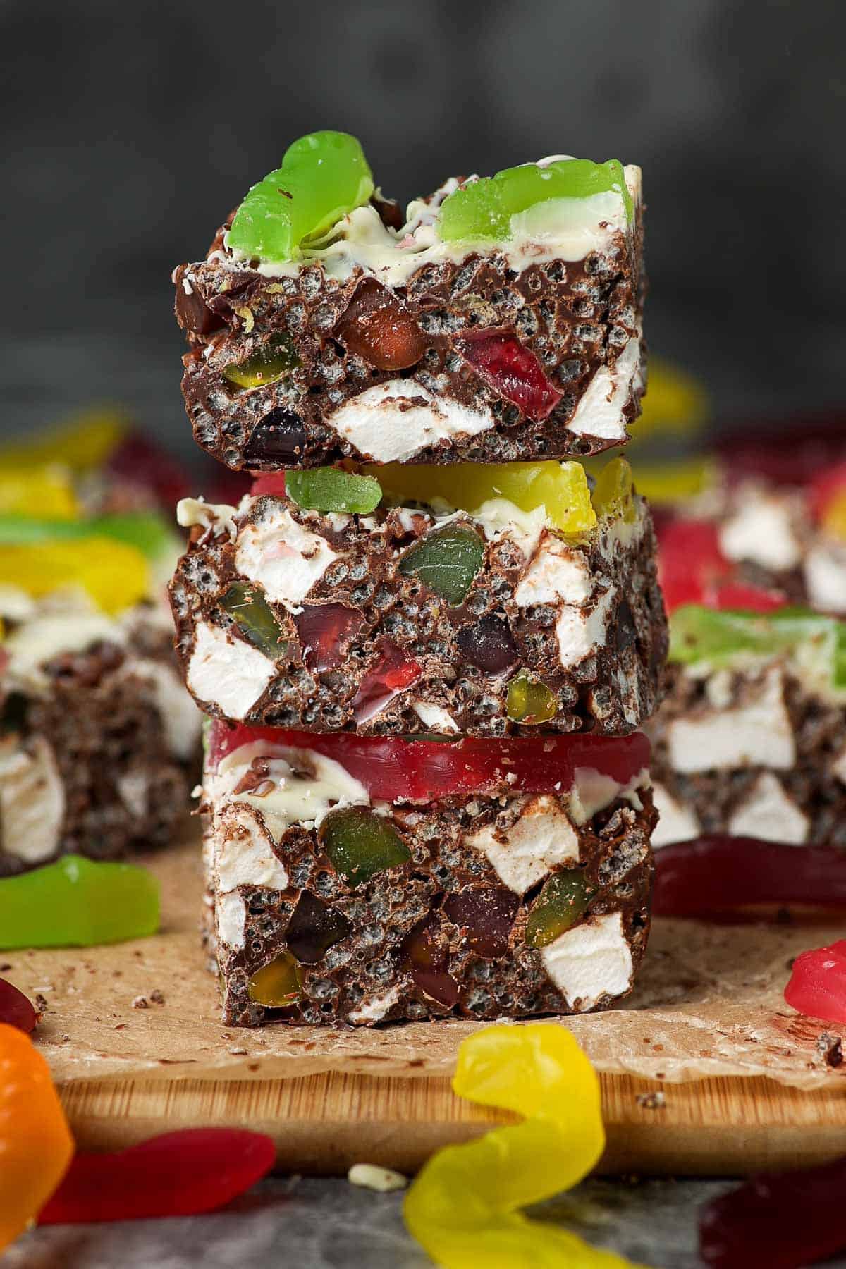 Stack of three pieces of rocky road, sitting on a wooden board.