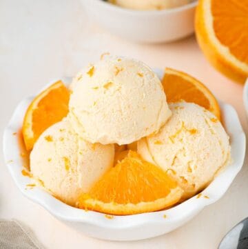 Round white bowl of ice cream with three scoops and some orange pieces.