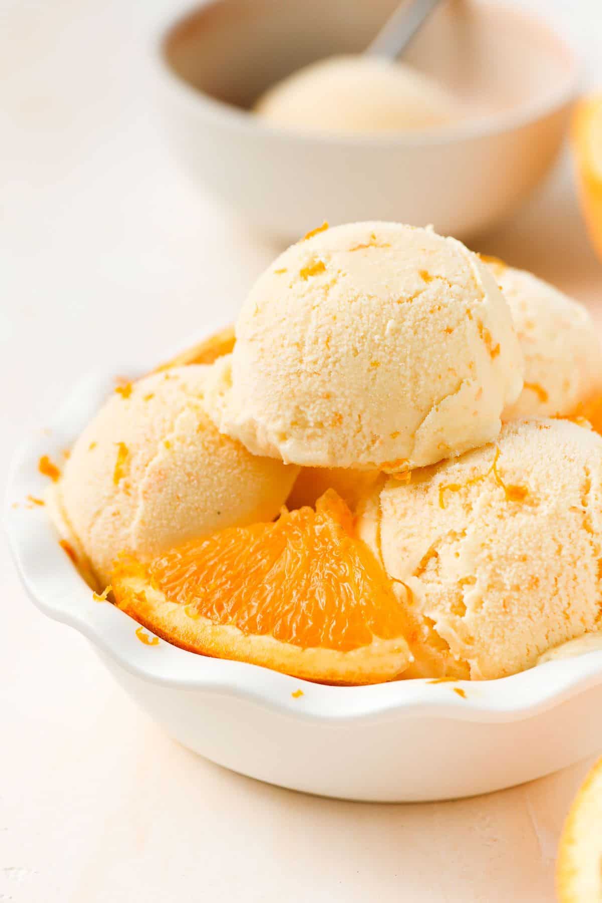 Round white bowl of ice cream with four scoops and some orange pieces.