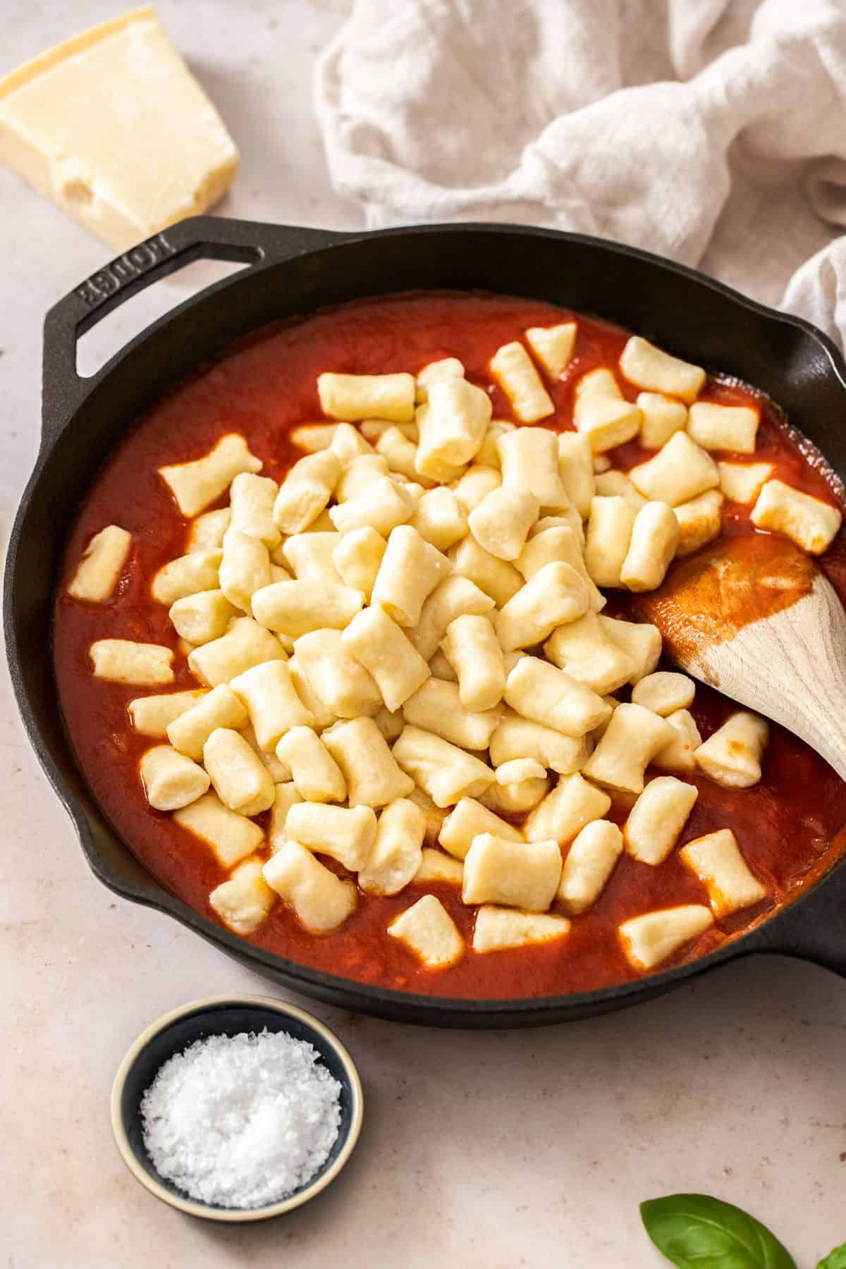Skillet with a tomato sauce and the ricotta gnocchi sitting on top, with a wooden spoon about to combine them.
