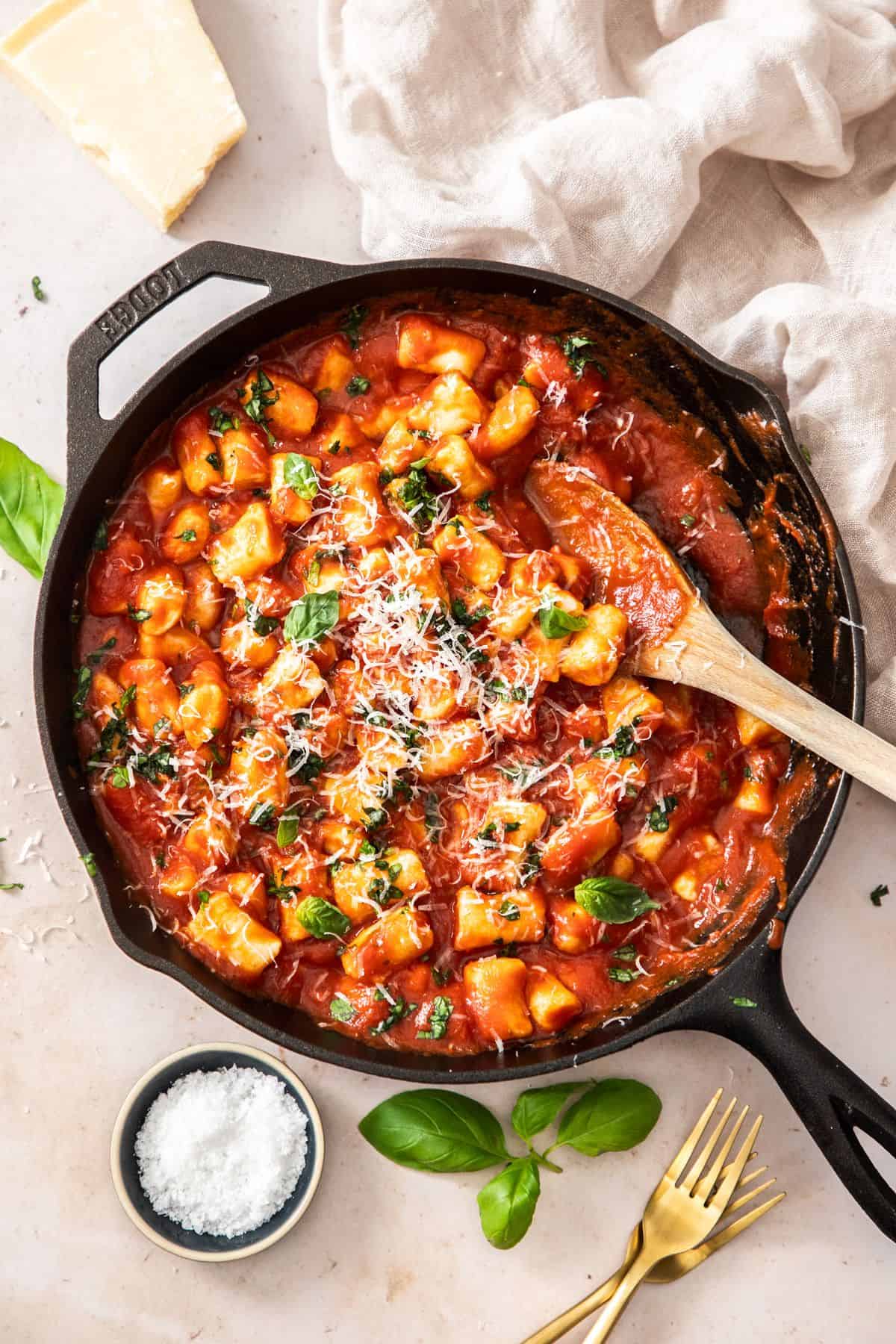 Skillet with the cooked gnocchi in a tomato sauce, ready to be served with a wooden spoon.