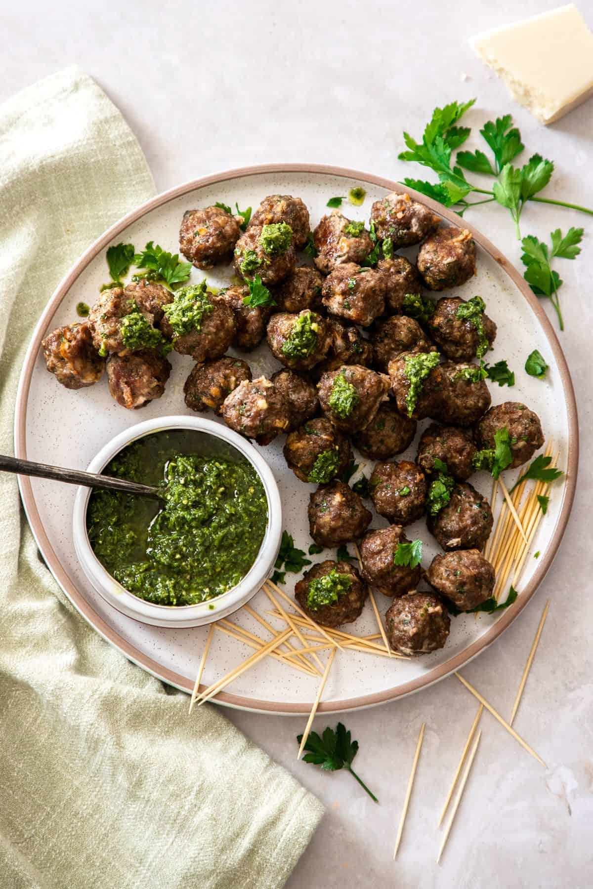Round plate of meatballs, with a bowl of pesto on the edge and some toothpicks.