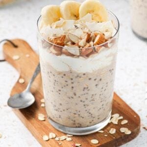 Glass jar of overnight oats, sitting on a wooden board, with a spoon on the edge.