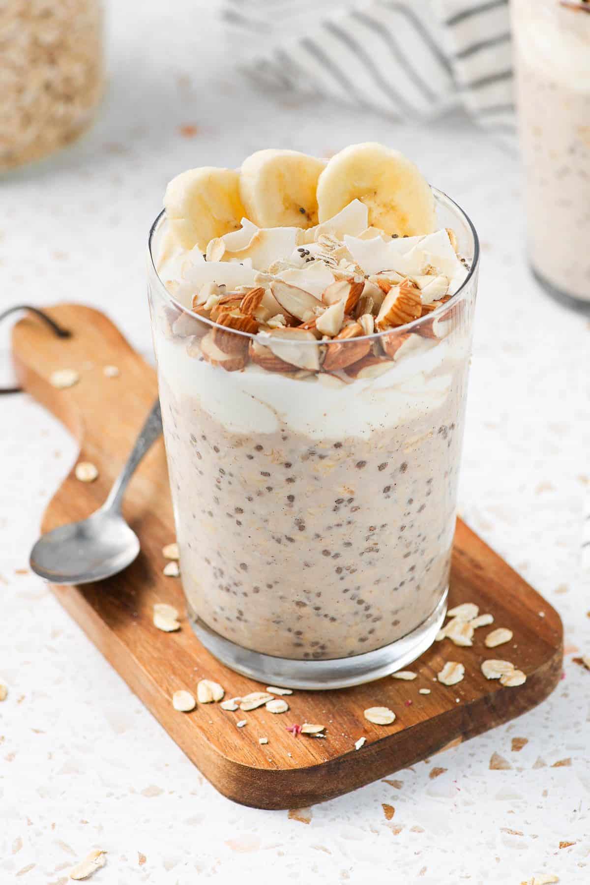Glass jar of overnight oats, sitting on a wooden board, with a spoon on the edge.