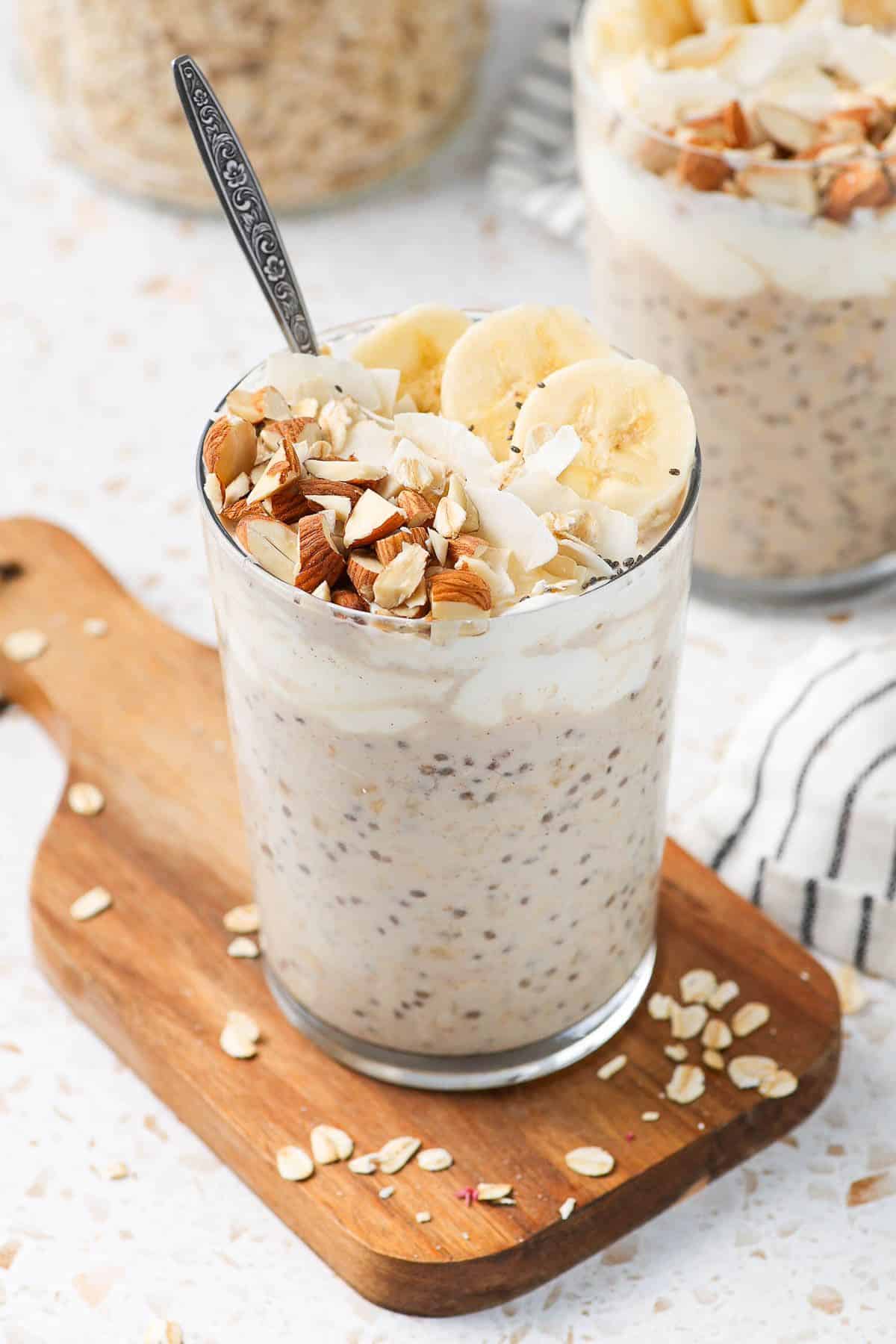 Glass jar of overnight oats, sitting on a wooden board, with a spoon in the jar.