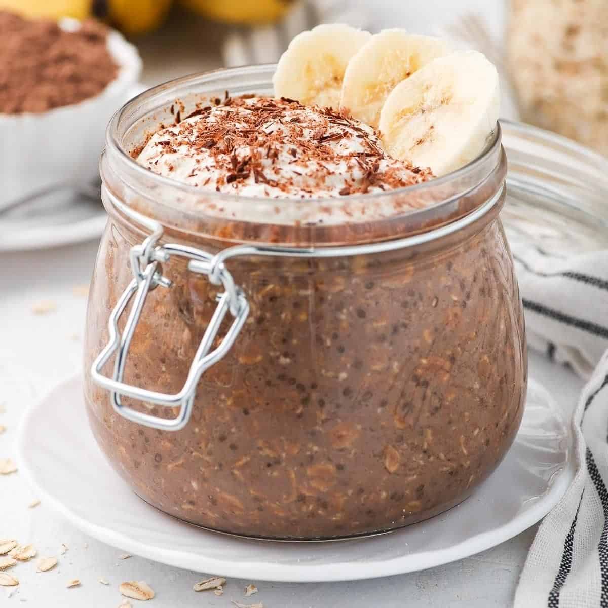 Jar of oats, topped with yoghurt, slices of banana and shaved chocolate.