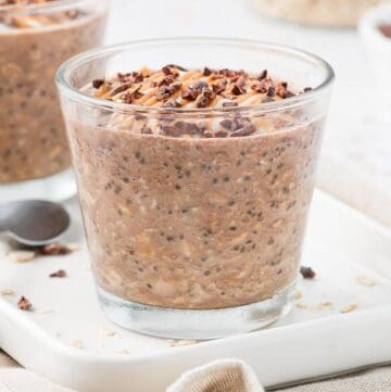 Jar of overnight oats, sitting on a white plate, garnished with peanut butter and cacao nibs.