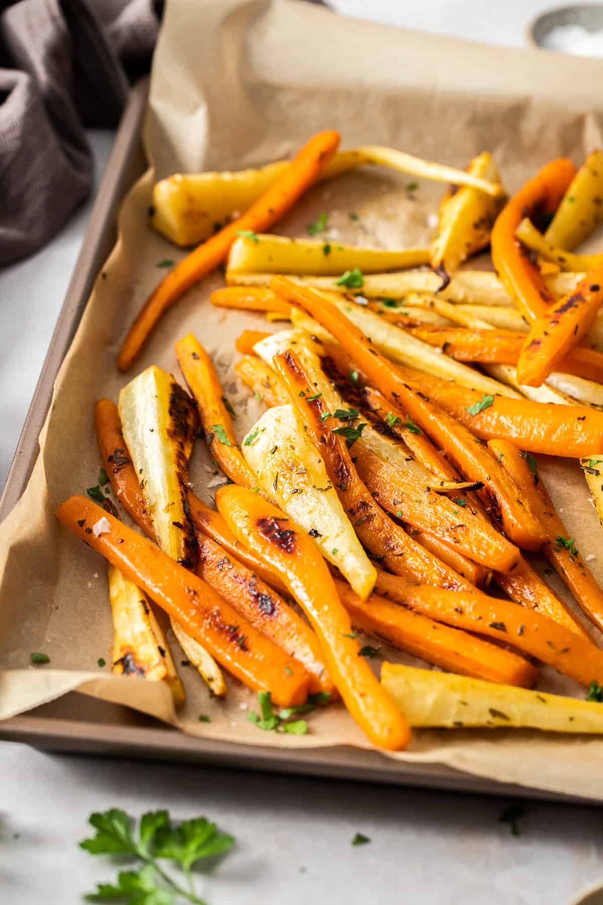 Baking tray with roasted carrots and parsnips, garnished with some fresh parsley.