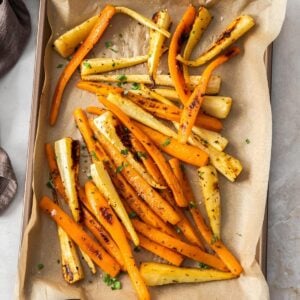 Baking tray with roasted carrots and parsnips, garnished with some fresh parsley.