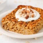 Slice of baked oats on a round white plate, topped with yoghurt and chopped almonds.