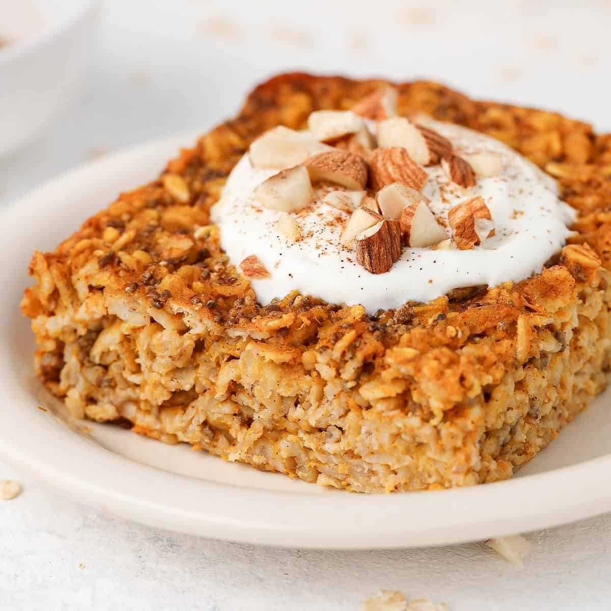 Slice of baked oats on a round white plate, topped with yoghurt and chopped almonds.