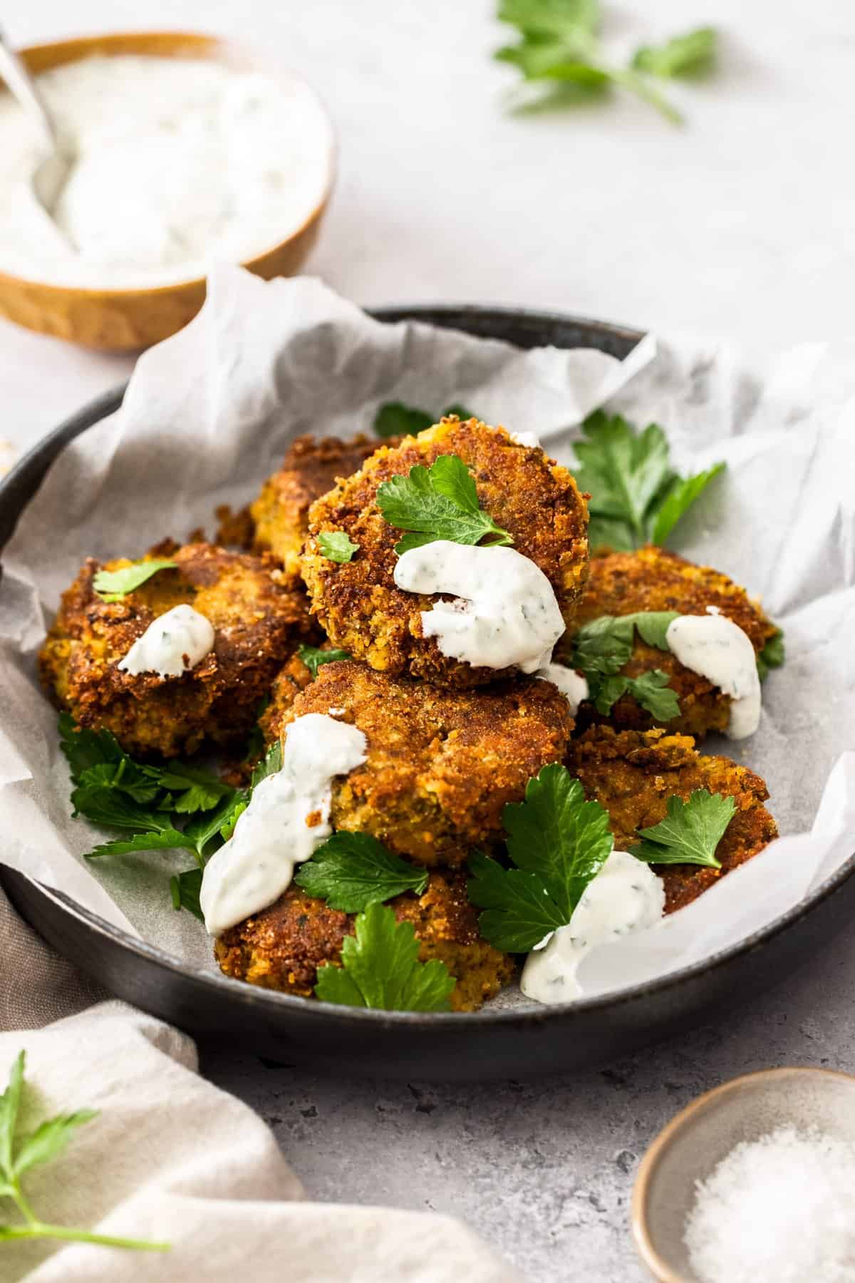 Round dish of cooked patties sitting on some baking paper, garnished with parsley and some yoghurt sauce.