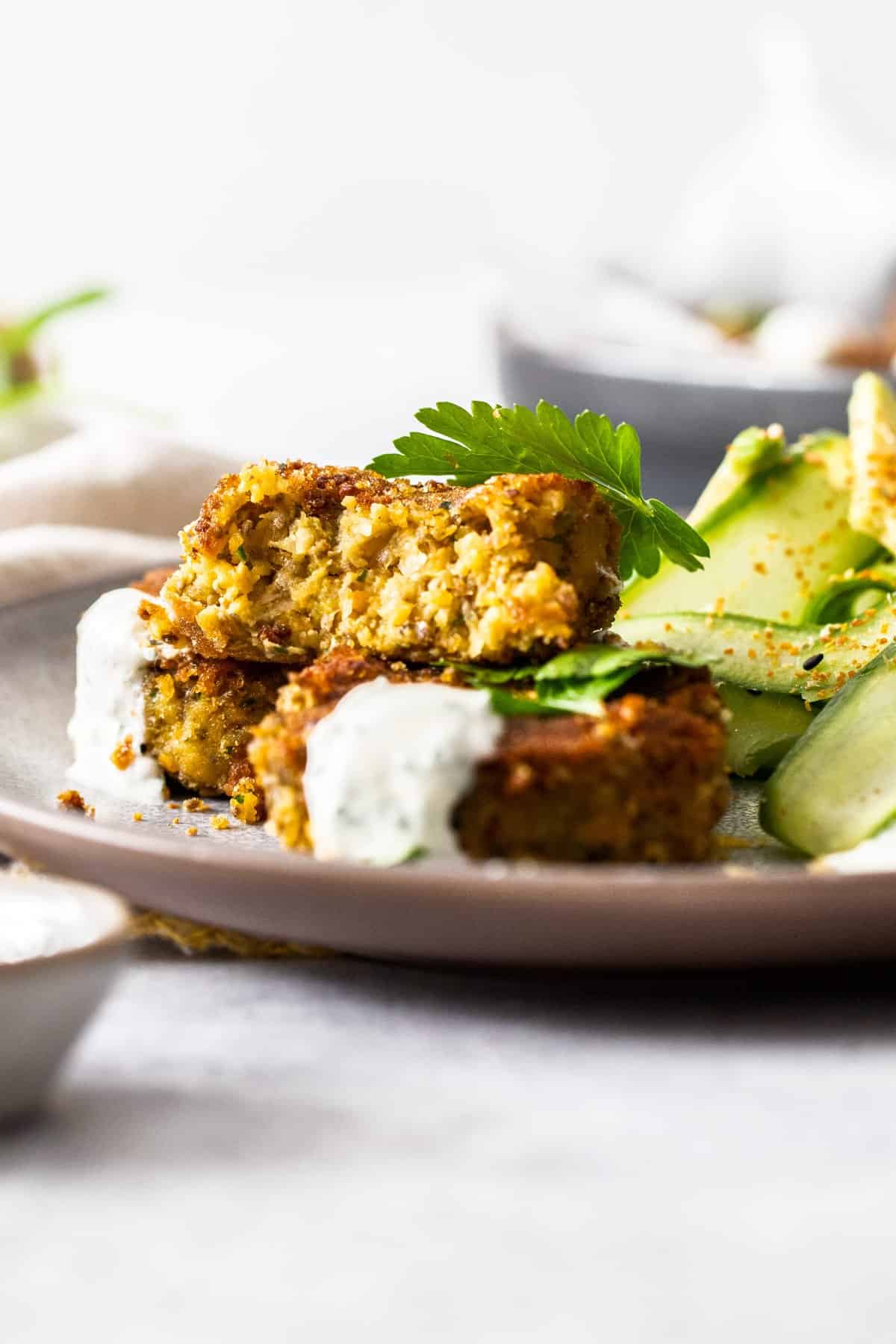 Plate of patties, one cut in half, garnished with some yoghurt sauce and some cucumber salad on the side.