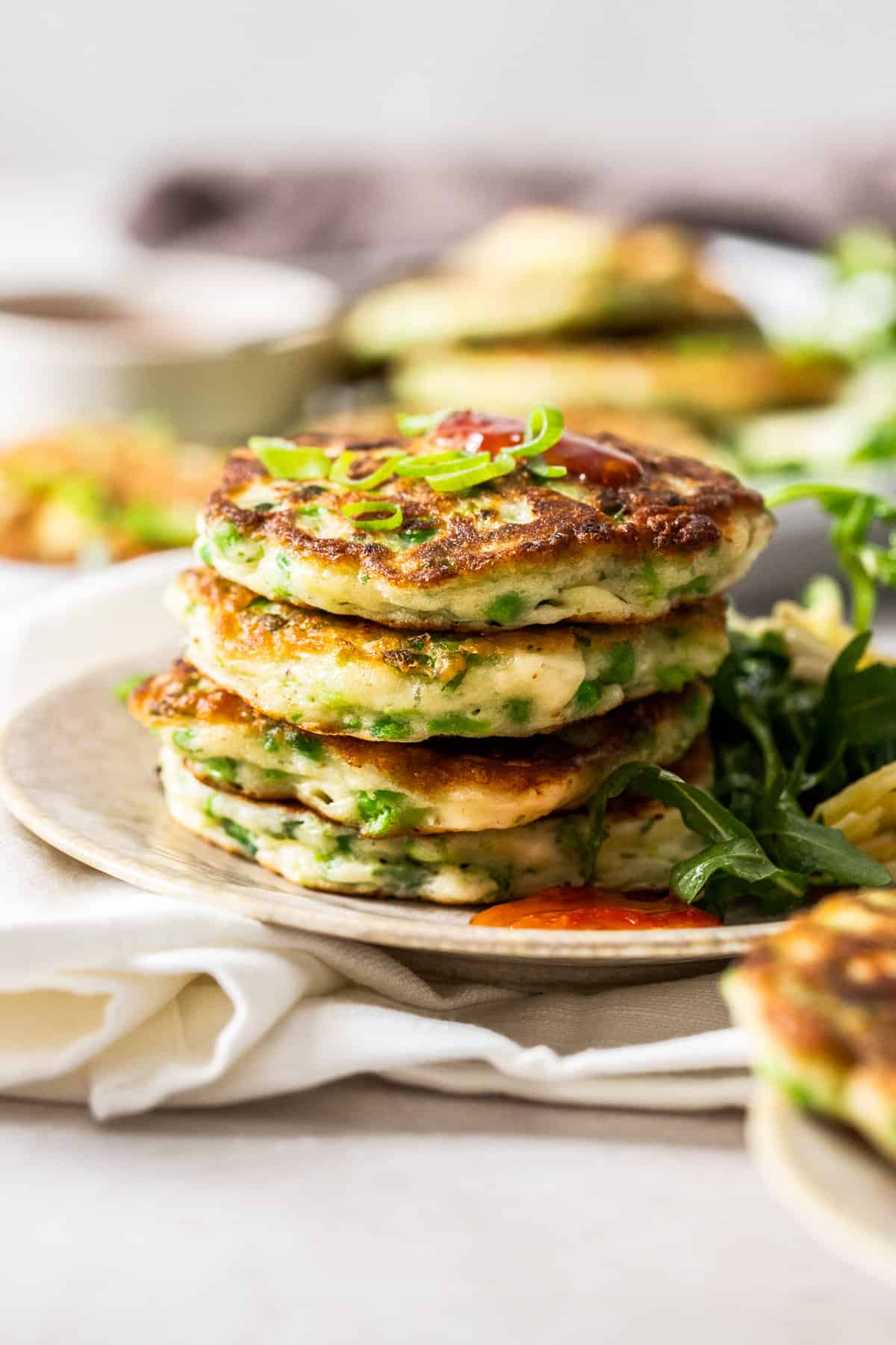 Stack of fritters on a plate, with some chilli sauce and rocket salad on the edge.